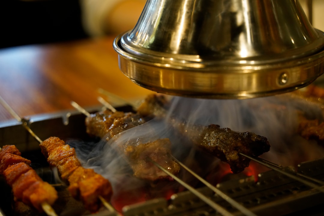 Skewers grilling over glowing charcoal under an extractor hood in a restaurant robata setup